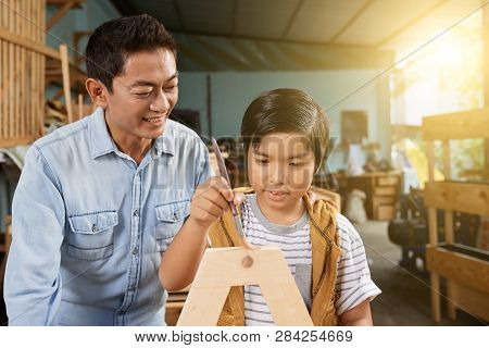 Smiling Mature Vietnamese Man Proudly Looking At His Son Applying Finishing Coat Of Laquer On Wooden
