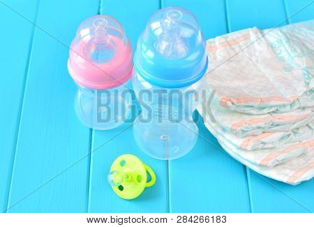 Newborn Child Stuff On A Wooden Background. Stack Of Baby Disposable Diapers, Pacifier And Feeding B