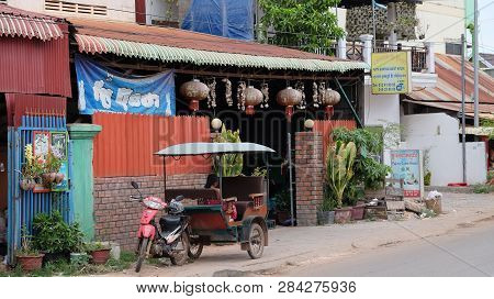 Cambodia, Siem Reap 12/08/2018 A Little Asian Girl Sits In A Moto Rickshaw Near A House With Red Lan