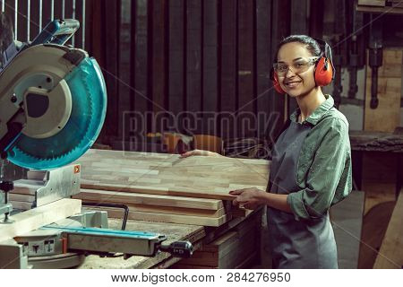 Smiling Craftswoman Grinding Timbers With Special Machine. Beautiful Woman Wearing Safety Glasses. C
