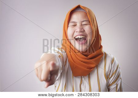Portrait Of Muslim Lady Wearing Hijab Laughing Hard And Pointing Forward, Bully Expression, Close Up
