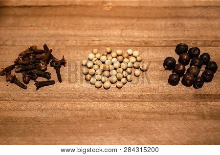 Small Piles Of Cloves, White Pepper Seeds And Juniper On The Wooden Background