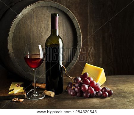 Bottle Of Red Wine With Glass And Cheese On Wooden And Barrel Background.