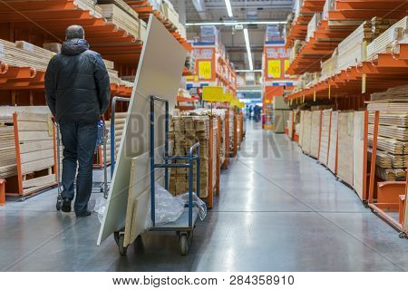 A Man In A Hardware Store. Carts Loaded With Boards. Shop Of Building Materials. Racks With Boards, 