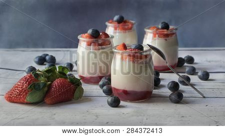 Homemade Yogurt With Strawberry Jam Under And Pieces Of Berries, On A White Wooden Board