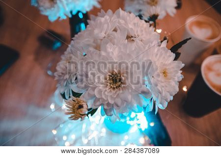 Lights Shining Behind The Bouquet Of White Fresh Flowers. Top View On The Decoreted Wooden Table. La