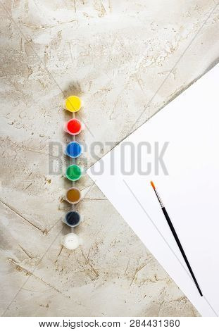 Flatlay With Bright Paints In Small Round Containers, Brush And White Sheet Of Paper On Grey Cement 
