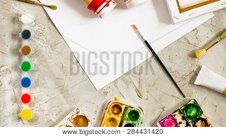 Flatlay With Bright Paints In Small Round Containers And Many Palettes, Brush And White Sheet Of Pap