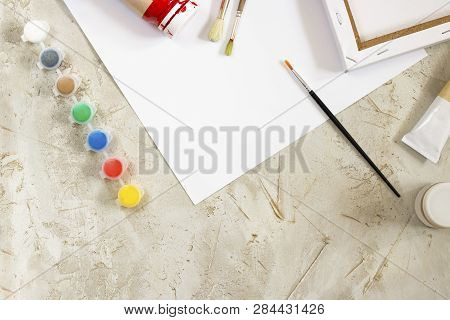 Flatlay With Bright Paints In Small Round Containers And Many Palettes, Canvas, Brush And White Shee