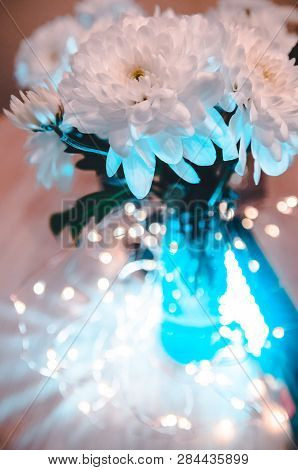 Lights Shining Behind The Bouquet Of White Fresh Flowers. Top View On The Decoreted Wooden Table.