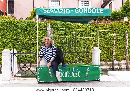 Venice, Italy-april 25, 2017: A Gondolier Waiting For Tourists Sits Under The Sign 