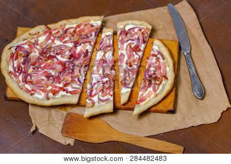 Alsatian Tart Flambé Or Flammkuchen With Bacon And Onions On A Dark Table.