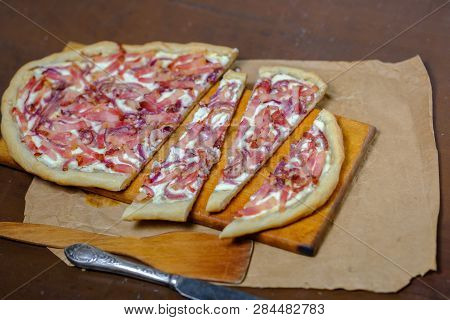 Alsatian Tart Flambé Or Flammkuchen With Bacon And Onions On A Dark Table.