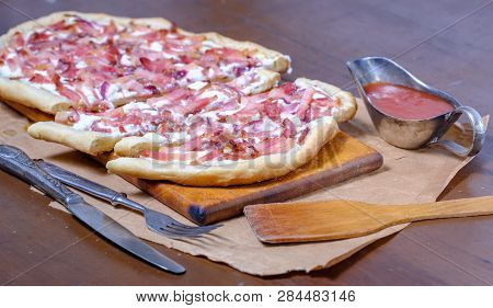 Alsatian Tart Flambé Or Flammkuchen With Bacon And Onions On A Dark Table.