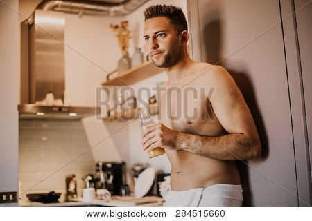 Attrctive Young Man With Bare Torso Holding Hand Orange Juice, Looking Out The Window And Smiling Wh