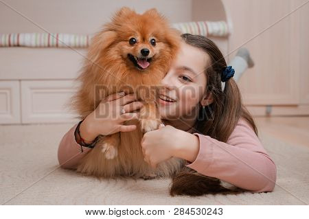 Teenage Girl With A Dog Breed Spitz Rejoices With A Pet At Home On The Floor. Care And Training Of A