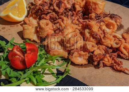 Crispy Fried Calamari Rings And Tentacles Served On A Rustic Board On A Piece Of Paper With Lemon We