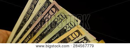 Banner Photo Of Dollar Bills Of Different Denominations In A Male Hand Against A Dark Background. Ca