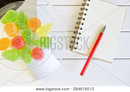 Multicolored Marmalade On Kitchen Scales Next To A Notebook And A Fountain Pen. Counting And Recordi