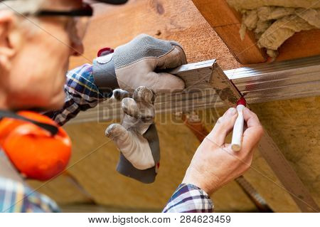 Man In Googles Making A Mark On Metal Frame On Unfinished Attic Ceiling. Attic Insulation And Renova