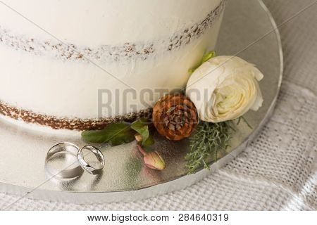 Closeup Picture About A Detail Of White Wedding Cake With Ornaments, With White Gold Wedding Bands