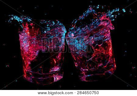 Colorfully Glowing Liquid Splashing From Two Rocks Glasses While They Toast On A Black Background