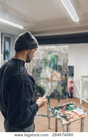 Portrait Of An Artist With Brushes In His Hands, Standing In An Art Studio On The Background Of An U
