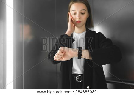 Young Woman In The Elevator Is Being Late. Junior Employee Is Looking At Her Watch Understanding She