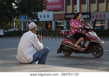 Turpan, China - August 10, 2012: A Han Chinese Woman Riding A Scooter And A Uyghur Man Sitting In A 