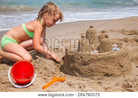 Little girl wearing green swimsuitbuilding a sand cactle on a sandy beach in Crete, Greece. Family summer vacation concept