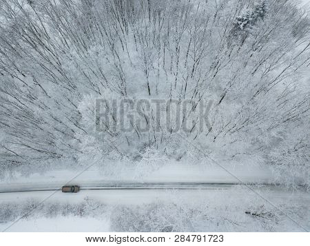 Aerial view of a car on winter road in the forest. Winter landscape countryside. Aerial photography of snowy forest with a car on the road. Captured from above with a drone. Aerial photo.