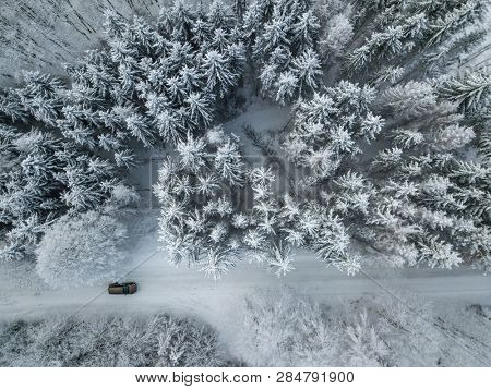 Aerial view of a car on winter road in the forest. Winter landscape countryside. Aerial photography of snowy forest with a car on the road. Captured from above with a drone. Aerial photo.