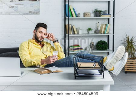 Thoughtful Bearded Businessman In Yellow Shirt Looking At Smartphone At Workplace