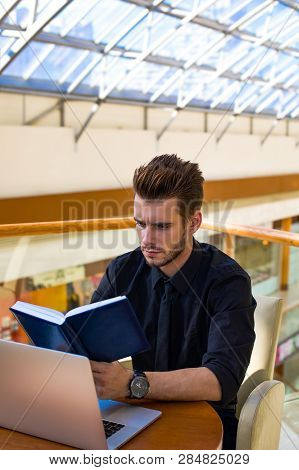 Young Modern Businessman Reading Information Form Textbook, Sitting Ta The Table With Open Laptop Co