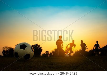 Silhouette Action Sport Outdoors Of A Group Of Kids Having Fun Playing Soccer Football On Green Gras