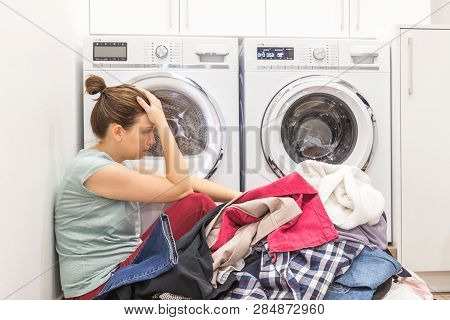 Upset Woman In Laudry Room Sitting Ona Floor With Dirty Clothes