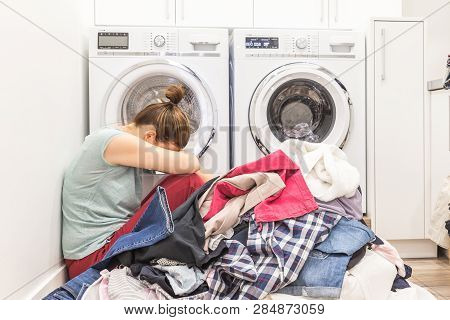 Upset Woman In Laudry Room Sitting Ona Floor With Dirty Clothes