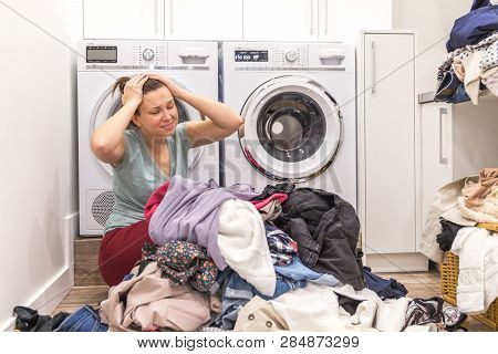 Upset Woman In Laudry Room Sitting Ona Floor With Dirty Clothes