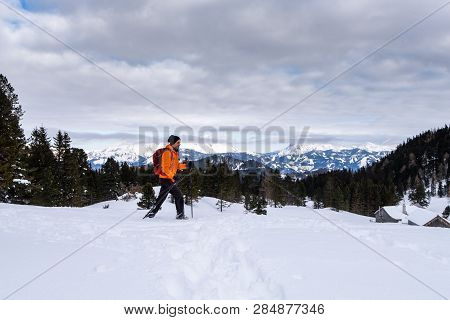 Man In Orange Jacket Snowshoeing On Scheibelalm In Holiday Resort Hohentauern With Panoramic View To