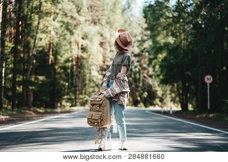 Lonely Traveler Girl With Backback Standing On Country Road. Traveler Girl Walking Along The Road To