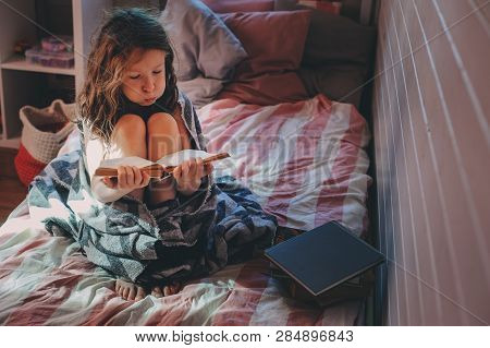 Thoughtful Kid Girl Reading Book Alone In Her Room In The Veening Or Early Morning