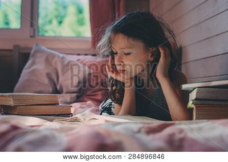 Thoughtful Kid Girl Reading Book Alone In Her Room In The Veening Or Early Morning
