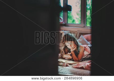Thoughtful Kid Girl Reading Book Alone In Her Room In The Veening Or Early Morning