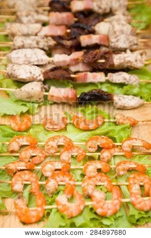 Skewers Of Shrimps On The Background Of Skewers With Chicken And Prunes. Skewers Lie On Lettuce Leav