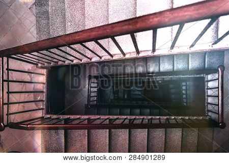 View From Above Of A Long Stairwell Going Down In A Spiral In An Antique Building With A Wooden Rail