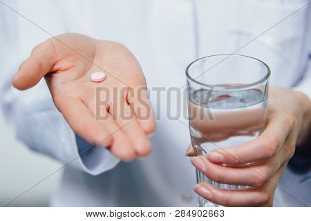 A Young Girl Doctor Takes Vitamins. At The Same Time, She Stands On A Gray Background Dressed In A W