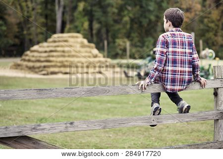 Boy Sitting On The Fence. Kid Having Fun At Farm. Copy Space For Your Text