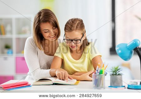 education, family and learning concept - mother and daughter doing homework together and reading book at home