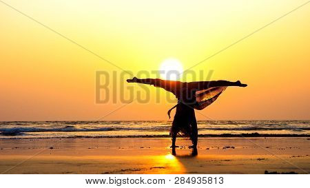 Silhouette Of Young Gymnast Woman Doing Handspring On Sandy Beach At Sunset