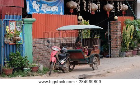 Cambodia, Siem Reap 12/08/2018 A Little Asian Girl Sits In A Moto Rickshaw Near A House With Red Lan